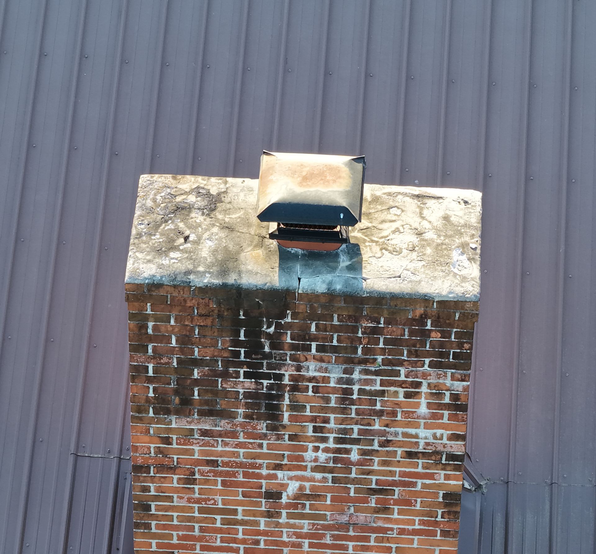 Close-up aerial photo of a cracked brick chimney on a metal roof documented during a roof inspection